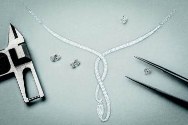 A diamond necklace and loose diamonds are arranged on a surface next to a caliper and tweezers, suggesting jewelry design or inspection.