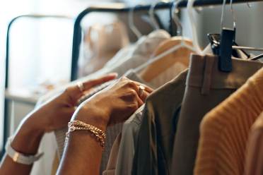 A person’s hands browsing clothes hanging on a garment rack.