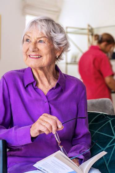 Elderly woman reading while carer cleans