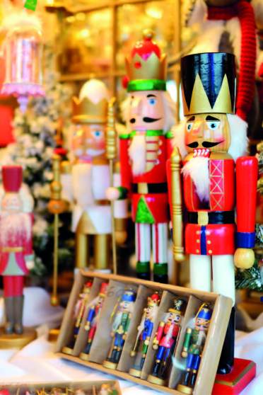 A display of various wooden nutcracker figurines and a small boxed set of miniature nutcrackers next to a snow-dusted artificial Christmas tree.