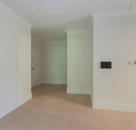 Empty room with beige carpet, off-white walls, white doors, and minimal fixtures. No furniture or decorations present. Ceiling light fitting is visible without a bulb.