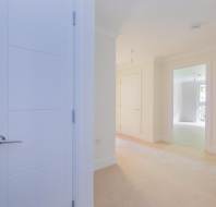 Bright, empty hallway in a modern home with beige carpet, white walls, and multiple open white doors leading to different rooms.