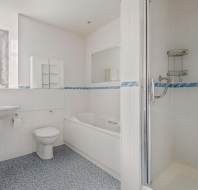 Bathroom with white tiled walls, featuring a shower stall, bathtub, toilet, and sink. There is a small window on the left side and a large mirror above the bathtub.