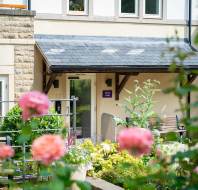 Entrance to a building with a black awning, bench, and garden with blooming pink flowers in the foreground.