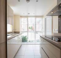 Modern kitchen with light-colored cabinets, electric cooktop, built-in oven, and large windows with vertical blinds letting in natural light.