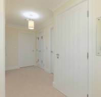 A hallway with cream walls, beige carpet, three closed white doors, a ceiling light, and a rectangular wall mirror.