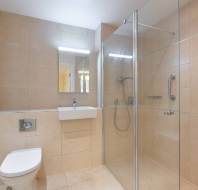 Modern bathroom with beige tiles, wall-mounted toilet, floating sink, glass-enclosed shower, and chrome grab bars.
