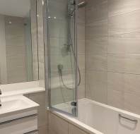 Modern bathroom with beige tiled walls, a rectangular sink with a mirror above, and a bathtub with a glass shower screen and wall-mounted showerhead.