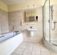 A modern bathroom featuring a bathtub, a wall-mounted sink with a mirror above it, and a glass-enclosed shower, with beige tiled walls and floor.