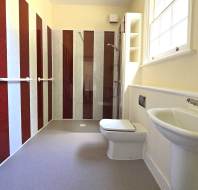 A bathroom with a toilet, sink, and shower area. The walls feature alternating red and white vertical stripes. There are grab bars near the shower and next to the toilet.