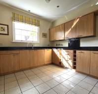A kitchen with wooden cabinets, black countertops, white tiled flooring, a window with yellow striped curtains, and wall-mounted shelves on the right.