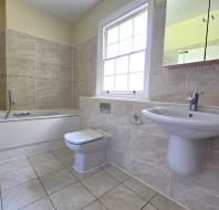 A clean, tiled bathroom with a bathtub-shower combo, a toilet, and a wall-mounted sink, illuminated by a window.