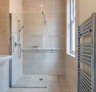A modern bathroom with beige tiles, a walk-in shower with a glass partition, a towel warmer rack, and a wall-mounted sink.