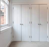 Two closed white cupboard doors next to a window in a carpeted room.
