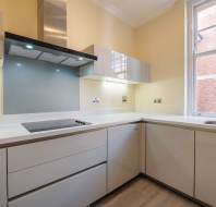 Modern kitchen with light-colored cabinets, an electric cooktop, a hood, and a window. A sink is on the right side.