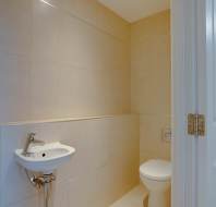 A small bathroom with beige tiled walls, featuring a wall-mounted sink and a toilet next to a partially open white door.