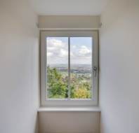 View through a rectangular window showing a scenic landscape with trees and clouds in the distance. White walls surround the window.