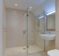 Modern bathroom featuring a glass-enclosed shower, wall-mounted sink, and toilet. Beige tiles cover the walls and floor, with a heated towel rail on one side.