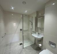 Modern bathroom with beige tiles, a glass-enclosed shower, a white sink, and a toilet. Ceiling lights illuminate the space.