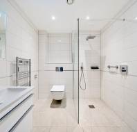 Modern bathroom with white tiles, a walk-in shower with a glass partition, a wall-mounted toilet, a sink with cabinet, and a heated towel rail.