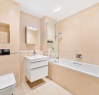 Modern bathroom with beige tiles, a bathtub with glass shower partition, a white vanity with a mirror, and a toilet.