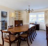 A dining room with a wooden table, eight chairs, a chandelier, shelves, a cabinet, and a door with glass panels.