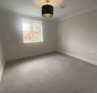 Empty room with gray carpet, white walls, and a single window with a view of a house. A black ceiling light fixture is centered on the ceiling.