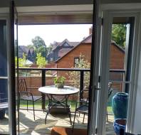 Balcony with a round table and two chairs overlooking a residential area with brick houses and trees.