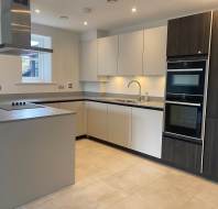 Modern kitchen with a central island, integrated oven, and stovetop. Cabinets are a mix of light and dark wood finishes. Room features tiled flooring and overhead lighting.