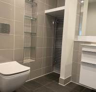 Modern bathroom with wall-mounted toilet, glass shelves, heated towel rail, and a white vanity.