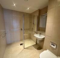 Modern bathroom with beige tiles, a glass-enclosed shower, a wall-mounted sink, and a toilet under soft lighting.