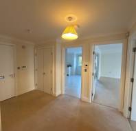 A hallway with beige carpet, white walls, and three open doors leading to different rooms. A ceiling light fixture is visible above.