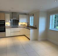 Modern kitchen with white cabinets, a built-in oven, and stainless steel appliances. Large windows provide natural light.