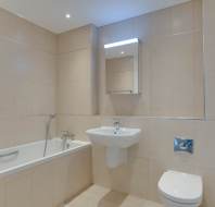 Modern bathroom with beige tiled walls, featuring a bathtub with a handheld shower, a wall-mounted sink, a toilet, and a mirror cabinet above the sink.