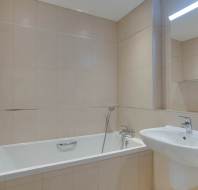 A bathroom with beige tiled walls, featuring a white bathtub with a handheld showerhead, a wall-mounted sink, and a mirror.