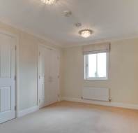 An empty room with beige carpet, white walls, a window with a blind, two ceiling lights, and closed double doors.
