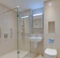 Modern bathroom with a glass-enclosed shower, beige tiled walls, a white wall-mounted sink, and a toilet.