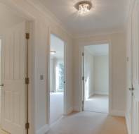 Interior hallway with open doors leading to three rooms; cream-colored walls and carpet; round ceiling light fixture.