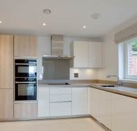 Modern kitchen with wood and white cabinets, built-in appliances, and a large window.