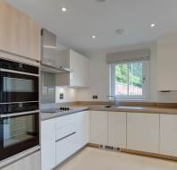 Modern kitchen with light wood and white cabinets, built-in appliances, and a small window with a view of greenery.