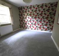 An empty room with gray carpet, green walls, and a polka dot accent wall. A window with patterned curtains is on the left, and a chandelier hangs from the ceiling.