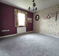 An empty room with purple walls, floral wallpaper on one wall, a window with patterned curtains, a ceiling light fixture, and gray carpet flooring.
