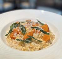 A plate of risotto topped with chunks of roasted pumpkin, sage leaves, and grated cheese.