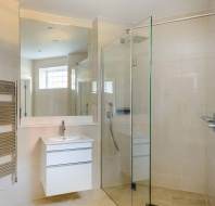 Modern bathroom with a glass shower, wall-mounted sink with vanity, large mirror, and towel rack. Beige tiles cover the walls and floor.