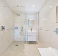 Spacious bathroom with white tiles, a walk-in shower, wall-mounted vanity, and a toilet.