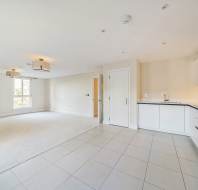 Spacious, unfurnished open-plan living room and kitchen with white walls and tile flooring, featuring large window and modern light fixtures.