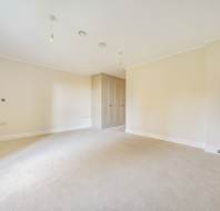 Empty room with beige walls, carpeted floor, and a built-in wardrobe. Two ceiling lights and recessed lighting are visible.