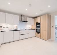 Modern kitchen with white cabinets, recessed lighting, and light wood accents. Includes built-in ovens and an adjoining laundry area with a washing machine.