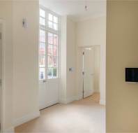 A bright room features large windows, a closed white door, a wall-mounted screen, cream-colored walls, and beige carpet.