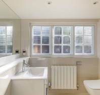 A clean, modern bathroom with a sink, toilet, large mirror, and window. Neutral tones and simple design.